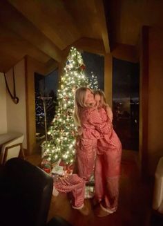 two girls standing in front of a christmas tree with their arms around each other's shoulders