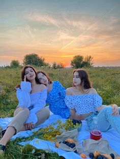 three young women sitting on a blanket in the grass at sunset, one with her eyes closed