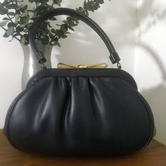 "1960s Granada USA Black Soft Vinyl Leather Top Handle Handbag, Vintage 60s Purse Classy 1960s Granada USA black soft vinyl leather top handle handbag that features: Gold tone metal hardware with a really pretty gold tone metal bow clasp closure that works well and closes tightly. Opens to a black satin lining with one interior side open pocket and one interior side metal zippered pocket. Stamped Granada USA There are protective feet on the bottom of the bag. Nearest mint condition *the exterior Mid-century Style Leather Evening Bag, Mid-century Leather Evening Bag, Vintage Top Handle Evening Bag, Retro Formal Shoulder Satchel, Vintage Leather Bag For Evening, Vintage Top Handle Shoulder Bag For Party, Vintage Evening Shoulder Bag With Top Carry Handle, Formal Black Satchel With Rolled Handles, Retro Leather Bags For Formal Occasions