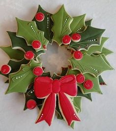 a decorated cookie wreath with holly leaves and red berries on it's side, sitting on a white surface