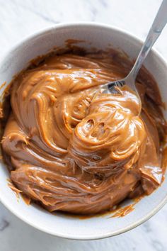 a white bowl filled with chocolate frosting on top of a marble counter next to a spoon