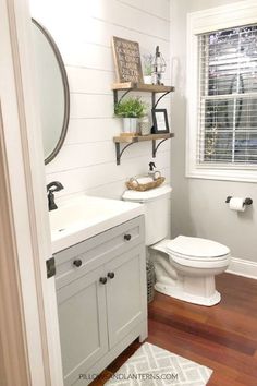 a white toilet sitting next to a sink in a bathroom under a window with wooden floors