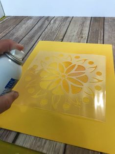 a person is using a spray paint to stencil a flower design on a piece of yellow paper