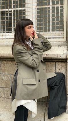 a woman sitting on the side of a building talking on a cell phone and holding her hand up to her mouth