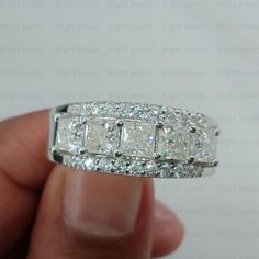 a hand holding a diamond ring in it's right hand, with the middle section partially surrounded by smaller diamonds