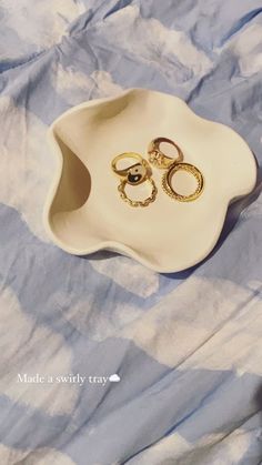 two gold rings sitting in a white bowl on a blue and white checkered cloth