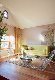 a living room filled with furniture and a large window next to a wooden floor covered in plants