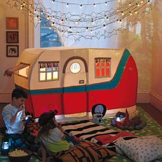 two children sitting on the floor in front of a camper shaped bed with lights strung above it