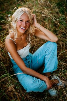 a beautiful blonde woman sitting in the grass with her hand on her head and smiling