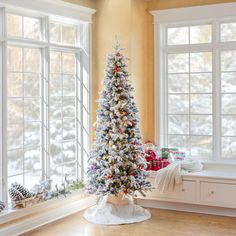 a decorated christmas tree in the corner of a room next to two windows with snow on them