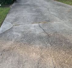 an empty driveway with grass and bushes in the background