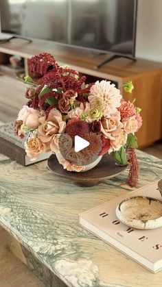 a vase with flowers on a table in front of a book and a television set