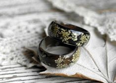 two rings sitting on top of a leaf next to each other in front of a lace doily