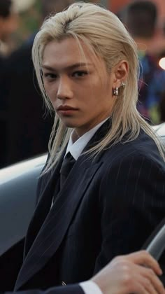 a woman with blonde hair sitting in a car wearing a suit and tie, looking at the camera