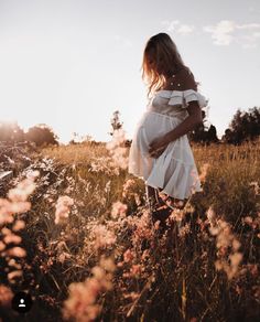 a pregnant woman is standing in the middle of a field with tall grass and wildflowers