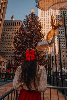 a woman standing in front of a christmas tree with a red bow on her head