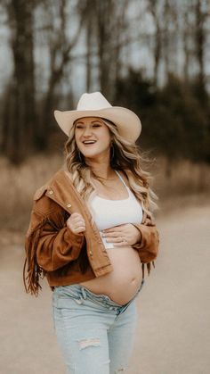 a pregnant woman in jeans and a cowboy hat is walking down the road with her belly exposed