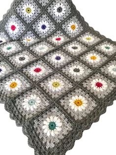 a crocheted granny granny blanket with flowers on the edge and bottom, sitting on a table