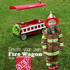 a little boy wearing a fireman's outfit standing next to a toy wagon