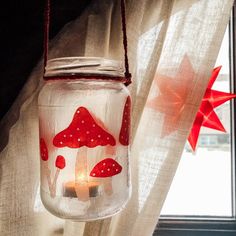 a glass jar with red mushrooms painted on it hanging from a window sill next to a star