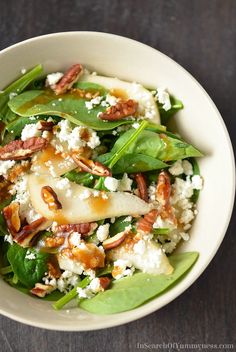 a white bowl filled with spinach, pears and feta cheese topped with pecans