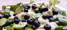 a salad with blueberries and cucumbers in it on a white plate sitting on a table