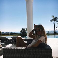 a woman sitting on top of a wicker chair next to a pool and palm trees