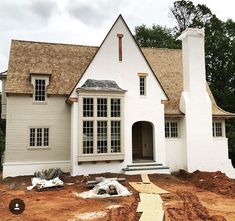 a white house is being built on the side of a dirt road in front of some trees