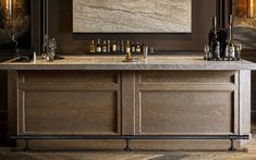 an elegant bar with marble counter tops and wine bottles on the top, surrounded by gold framed art work