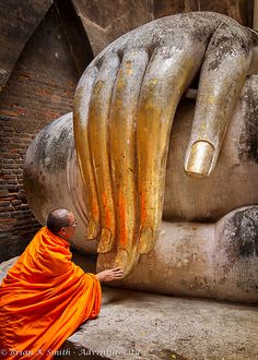 a man in an orange robe sitting next to a large statue with bananas on it