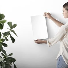 a woman holding up a white piece of paper next to a potted plant