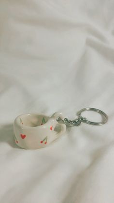 a tea cup shaped keychain with hearts on it sitting on a white sheet