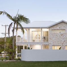 a white house with two balconies and palm trees in the front yard at dusk