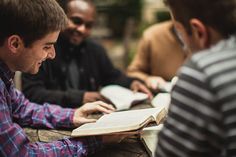 three men sitting at a table with an open book