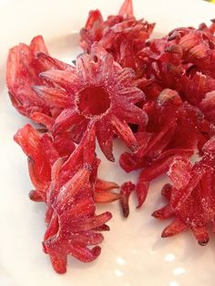 some red flowers on a white plate with water droplets all over the petals and leaves