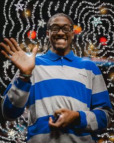 a man is smiling and holding his hand out in front of a christmas tree with lights