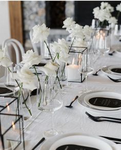 the table is set with white flowers in vases and place settings for dinner guests