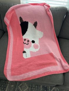 a pink crocheted blanket with a black and white cat on it sitting on a couch