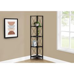 a black bookcase with four shelves in front of a window and framed pictures on the wall