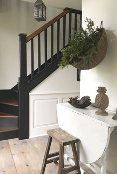 a wooden stool sitting in front of a stair case next to a table with pine cones on it