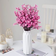 a white vase filled with pink flowers on top of a table