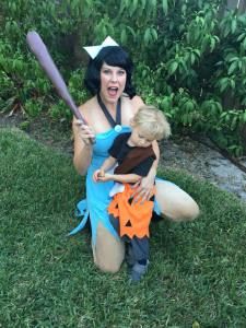 a woman holding a child in her arms while sitting on the grass with a baseball bat