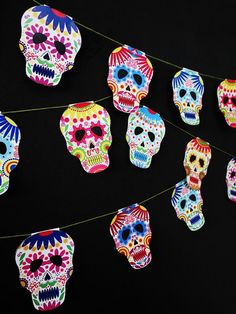 colorful sugar skulls are hanging from a string on a black background with yellow and red strings