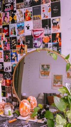 a mirror sitting on top of a table next to a potted plant in front of a wall covered with pictures