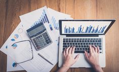 a person using a laptop computer on top of a desk with papers and calculator