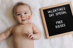 a baby laying next to a sign that says valentine's day special free kisses