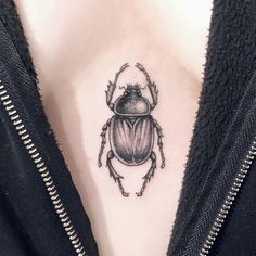 a beetle tattoo on the back of a woman's chest, with black ink