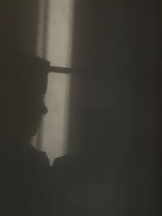 a man standing in front of a window with a hat on his head looking out the window