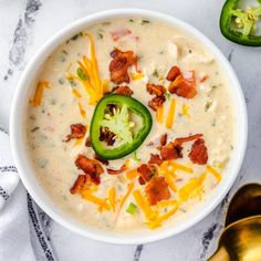 a white bowl filled with cheese, bacon and jalapeno peppers next to two spoons