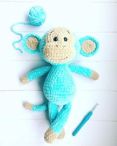 a crocheted monkey laying on the floor next to a ball of yarn and scissors